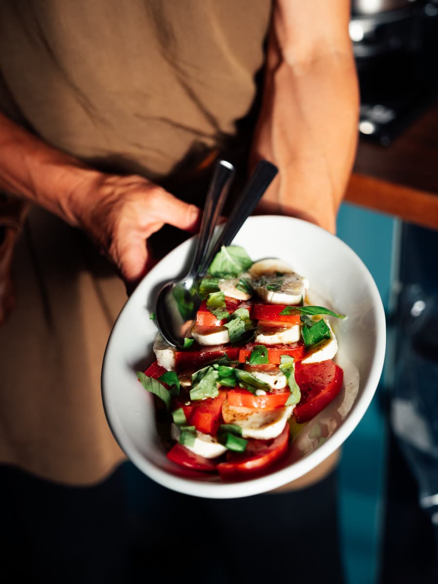 Ein Teller Caprese mit Tomaten, Mozzarella und Basilikum wird an den Tisch getragen