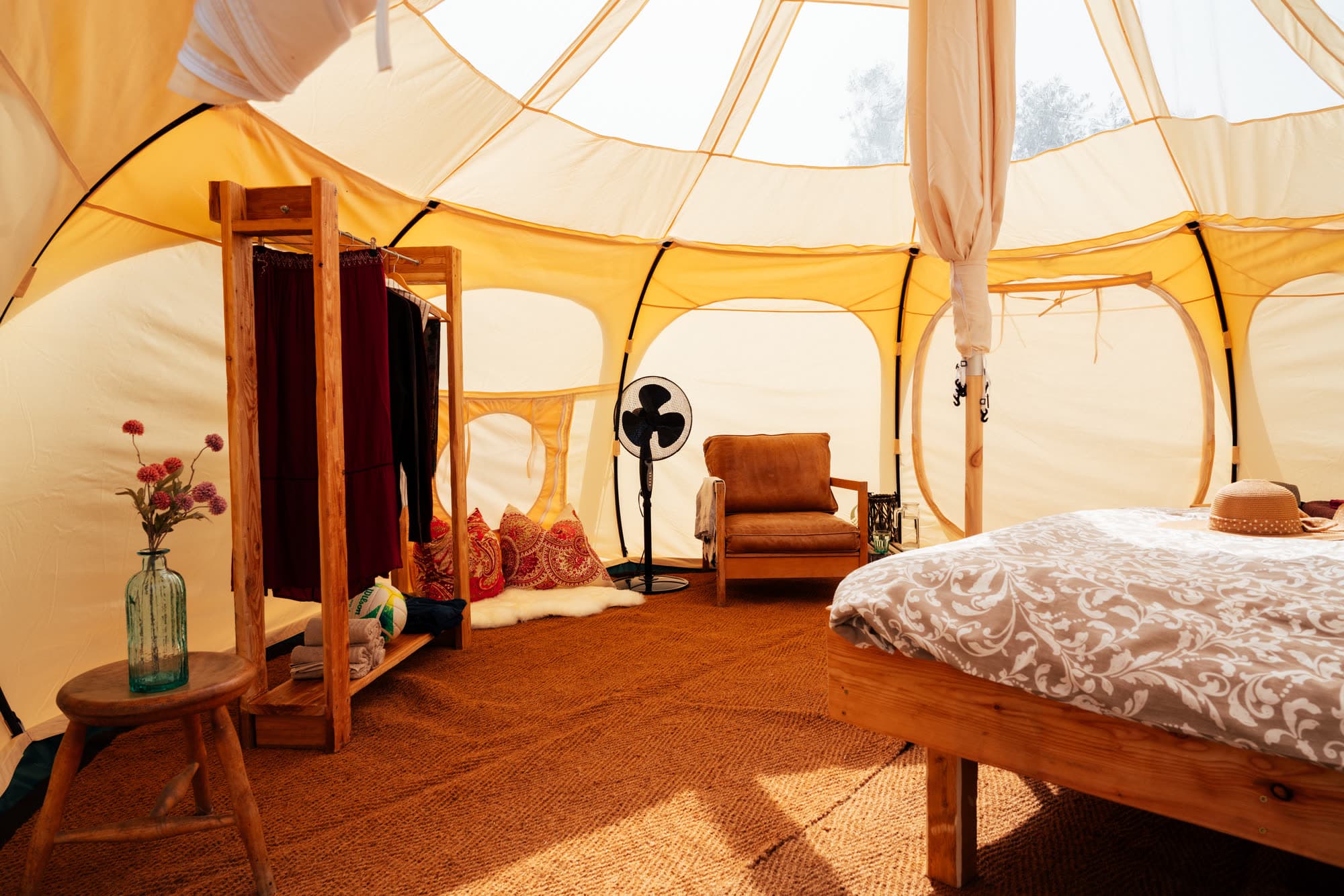 Inside the bell tent: double bed, leather armchair and clothes rail, with light and a view of the olive trees coming through the transparent roof panels
