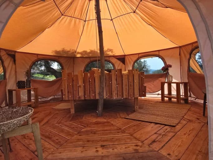 Inside the octagonal tent: wooden floor, a slatted wooden double bed with fairy lights and arched windows looking out into the olive grove