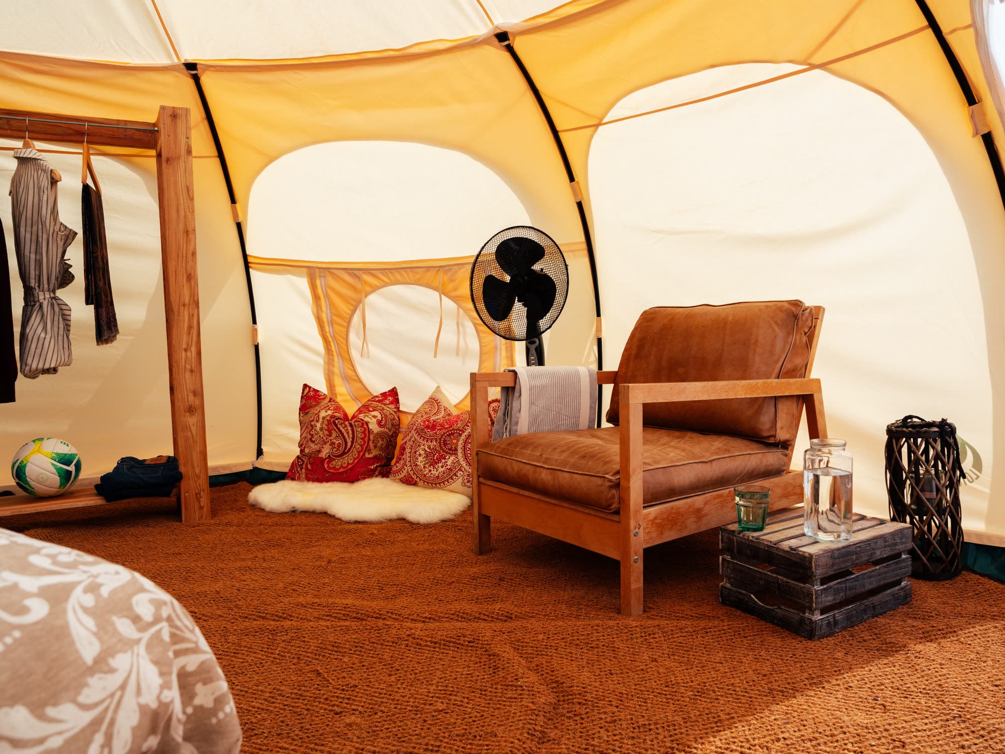 Seating corner in the tent with a brown leather armchair, a fan, paisley cushions and a wooden crate as a side table