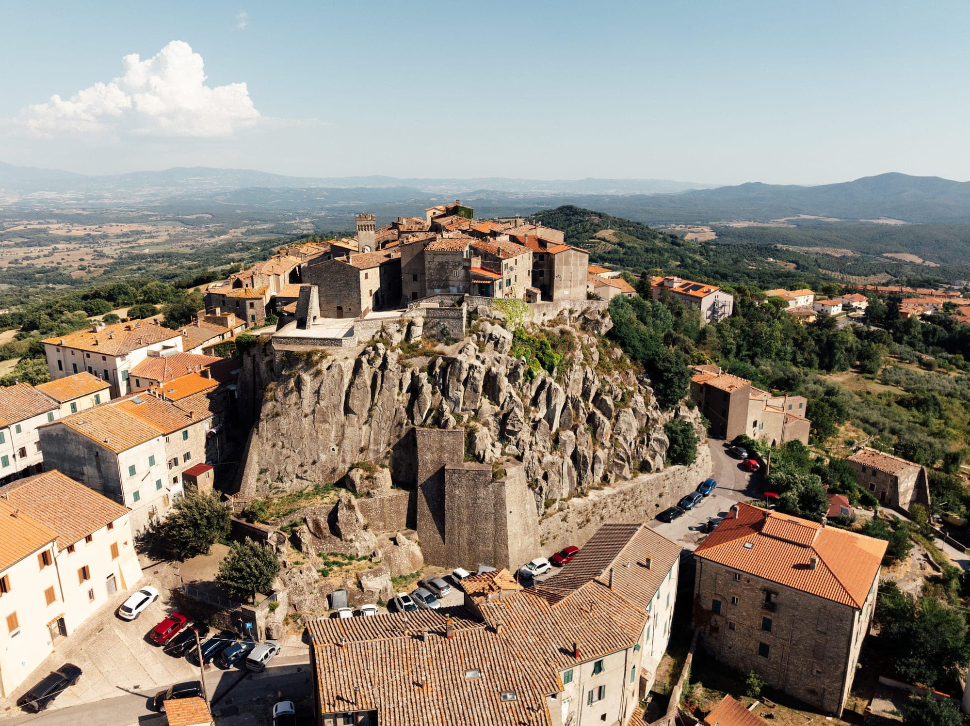 Roccastrada von oben: die Altstadt auf einem Felsen mit Uhrturm und Ziegeldächern, dahinter die Hügel der Maremma