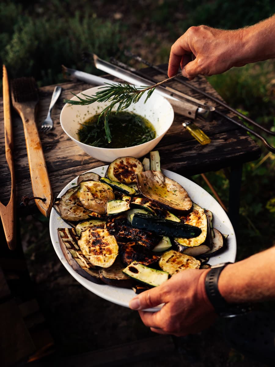 Tallerken med grillede grøntsager, der pensles med urteolie og en kvist rosmarin