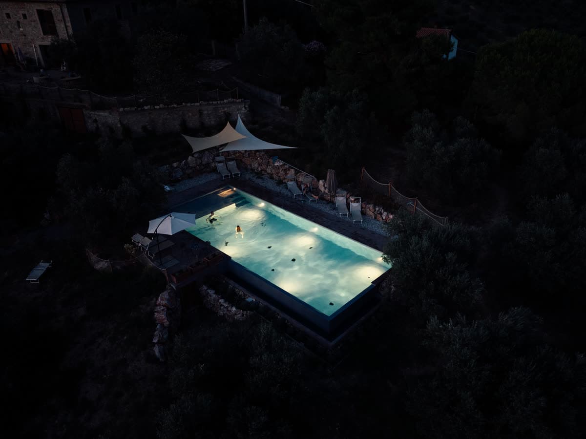 Den oplyste pool set oppefra om natten, omgivet af den mørke olivenskråning