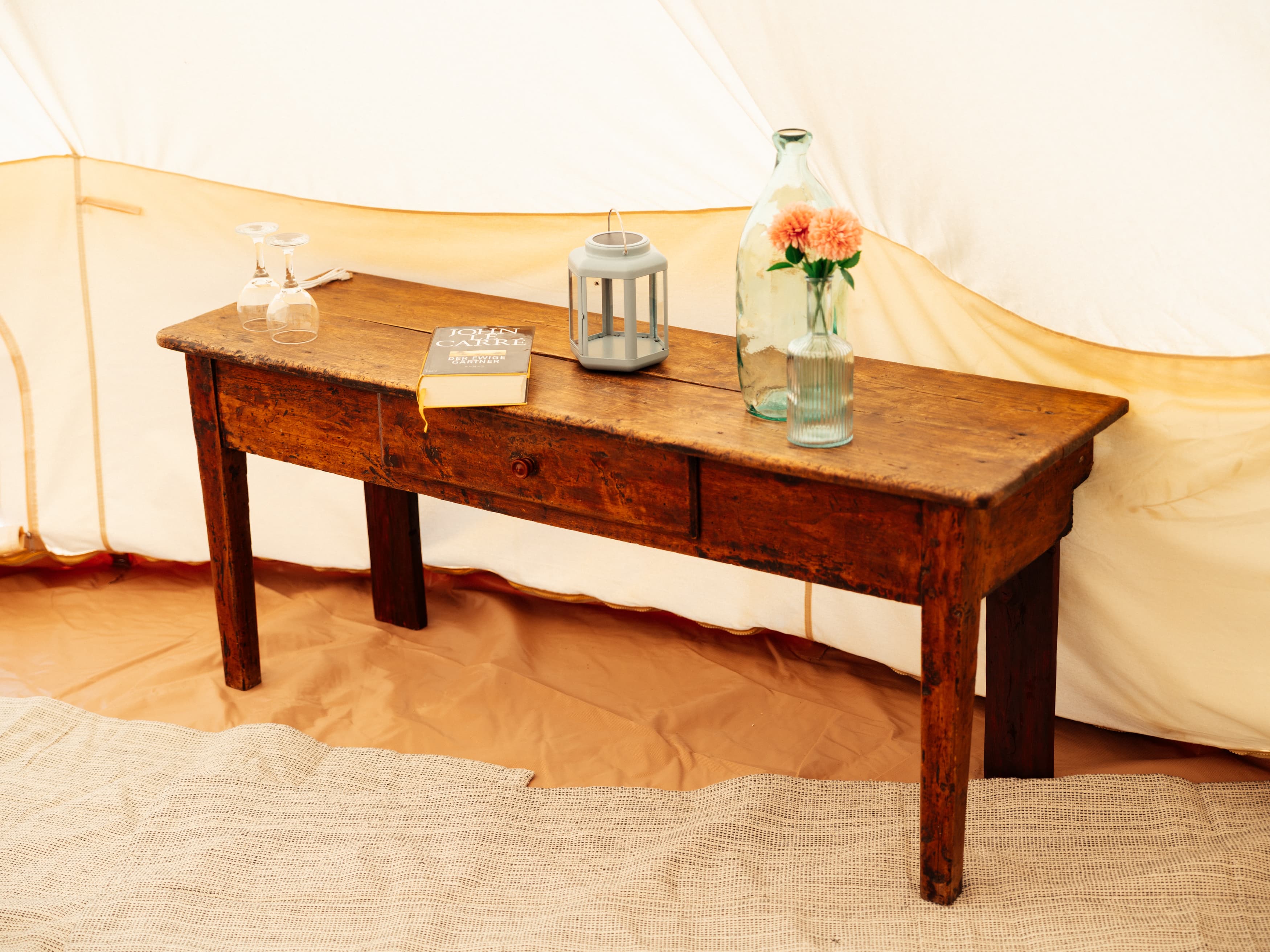 Old wooden table in the tent with a lantern, glasses, a book and a vase of flowers